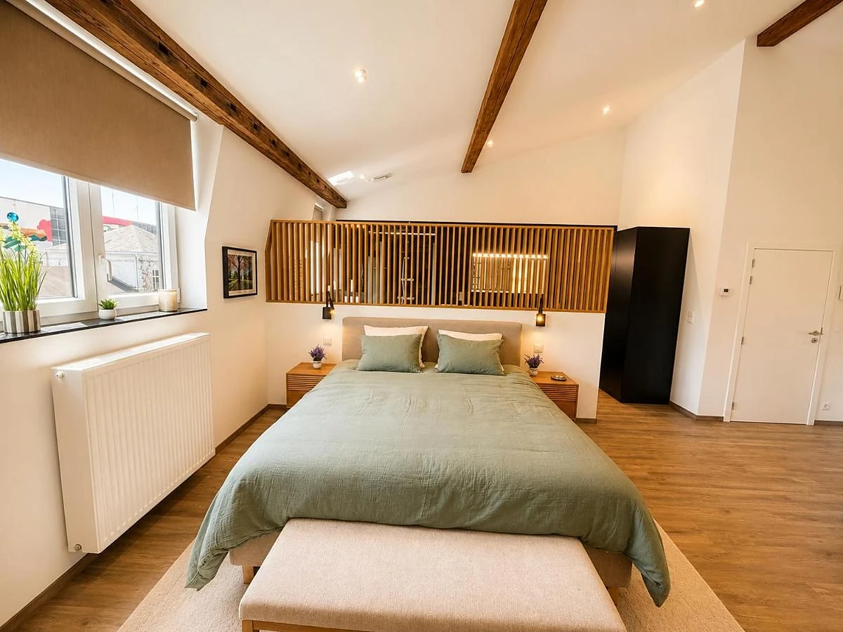 La suite : lit king-size vert sauge sous les poutres, tête de lit en bois